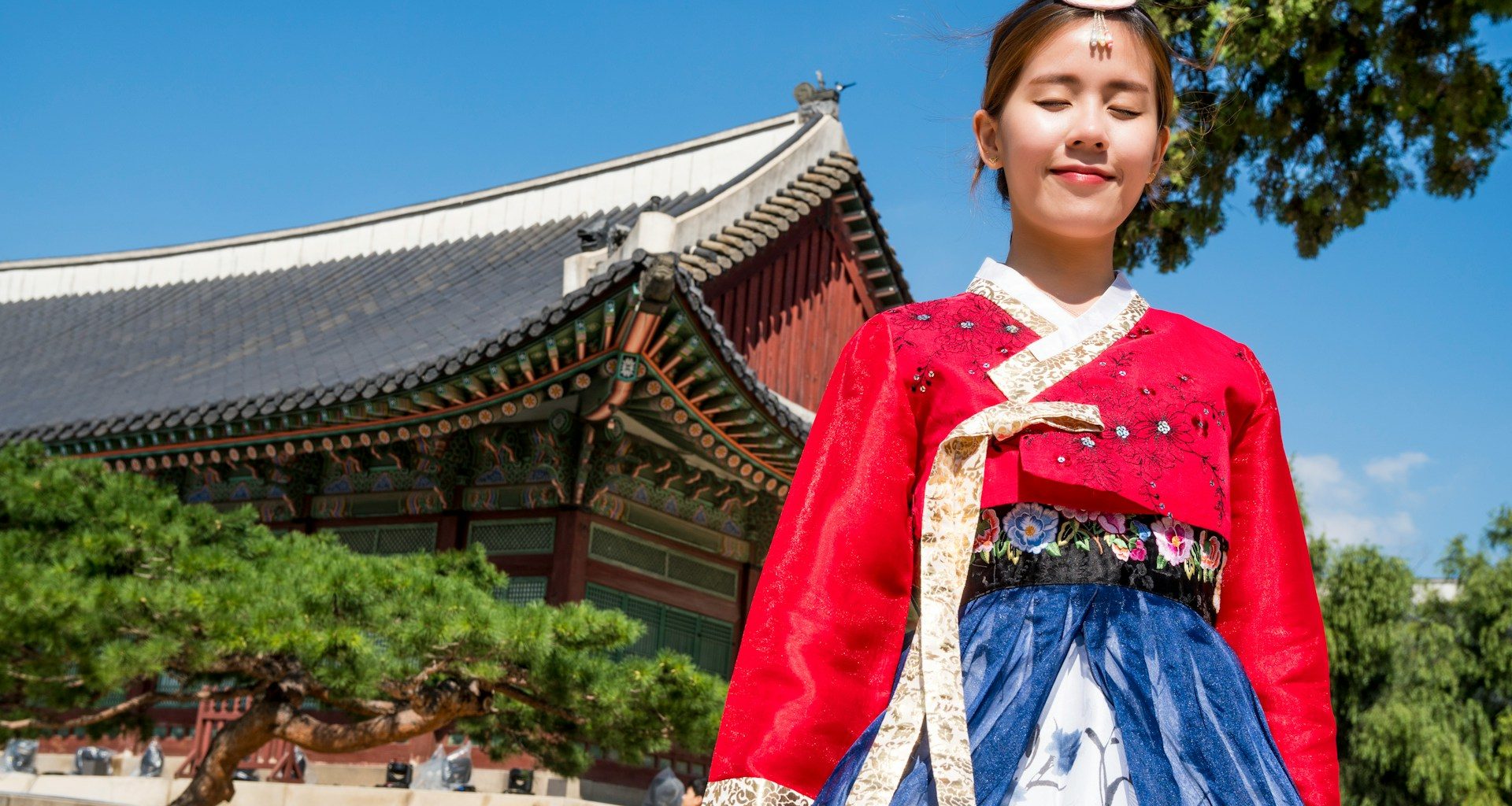 Young Korean woman in traditional hanbok, smiling with eyes closed in front of Gyeongbokgung Palace, South Korea.